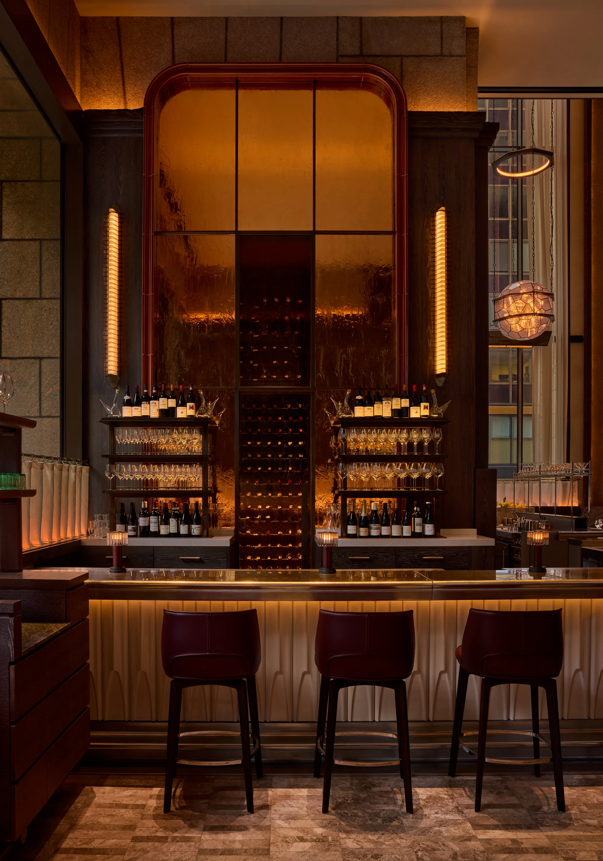 Low-lit bar with a metal bar top in front of a backlit wine display